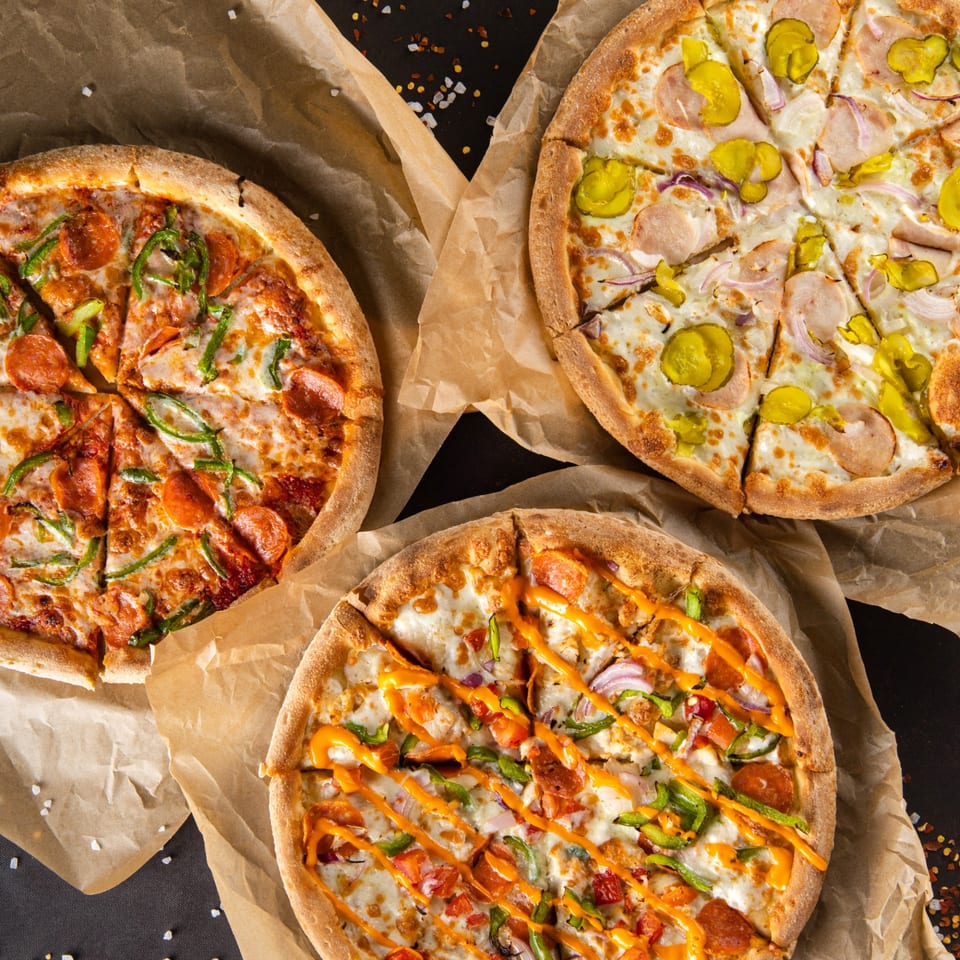 Three Popz Pizza pies, one pepperoni and green pepper, one with pickles, and one with orange sauce.